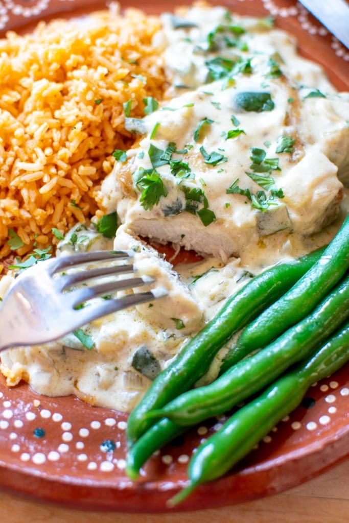 close up image of creamy cooked chicken with red rice and green beans on the side