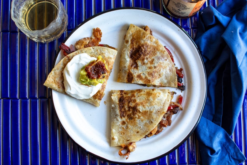 A chicken quesadilla on a white plate with a glass next to it.