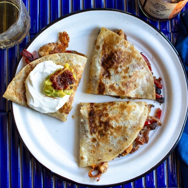 A chicken quesadilla on a white plate with a glass next to it.