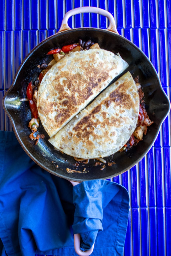 Two quesadillas in a skillet on a blue tile table