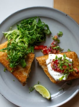 A chicken chimichanga on a plate topped with sour cream and salsa