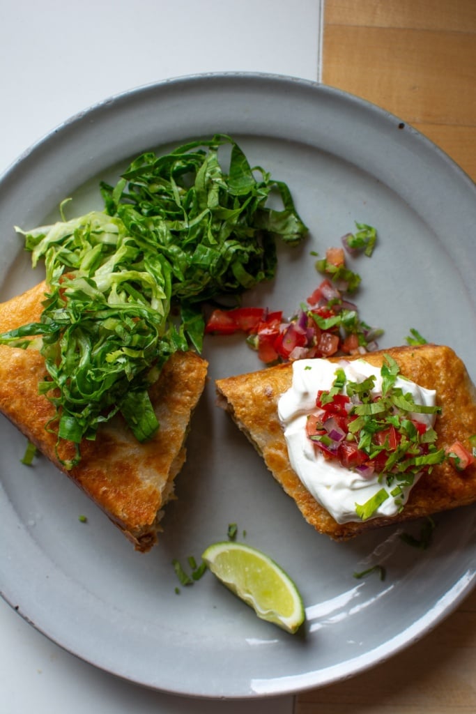 A chicken chimichanga on a plate topped with sour cream and salsa