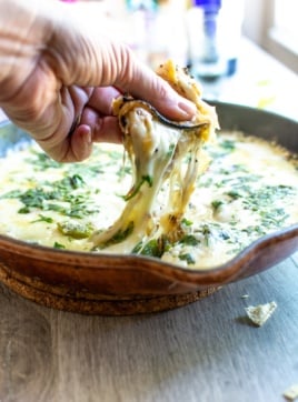 A hand dipping a corn tortilla into a batch of queso