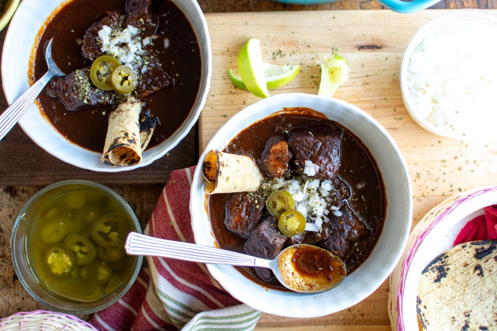 two bowls of Mexican red chili with a spoon in one bowl