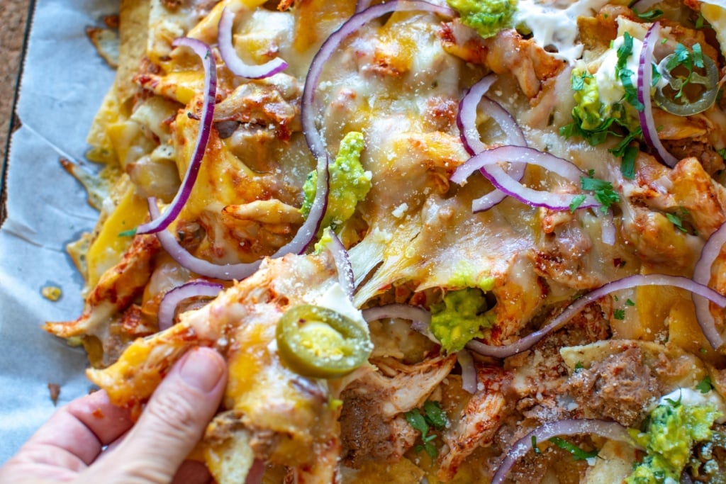 a sheet pan of nachos with one being pulled away