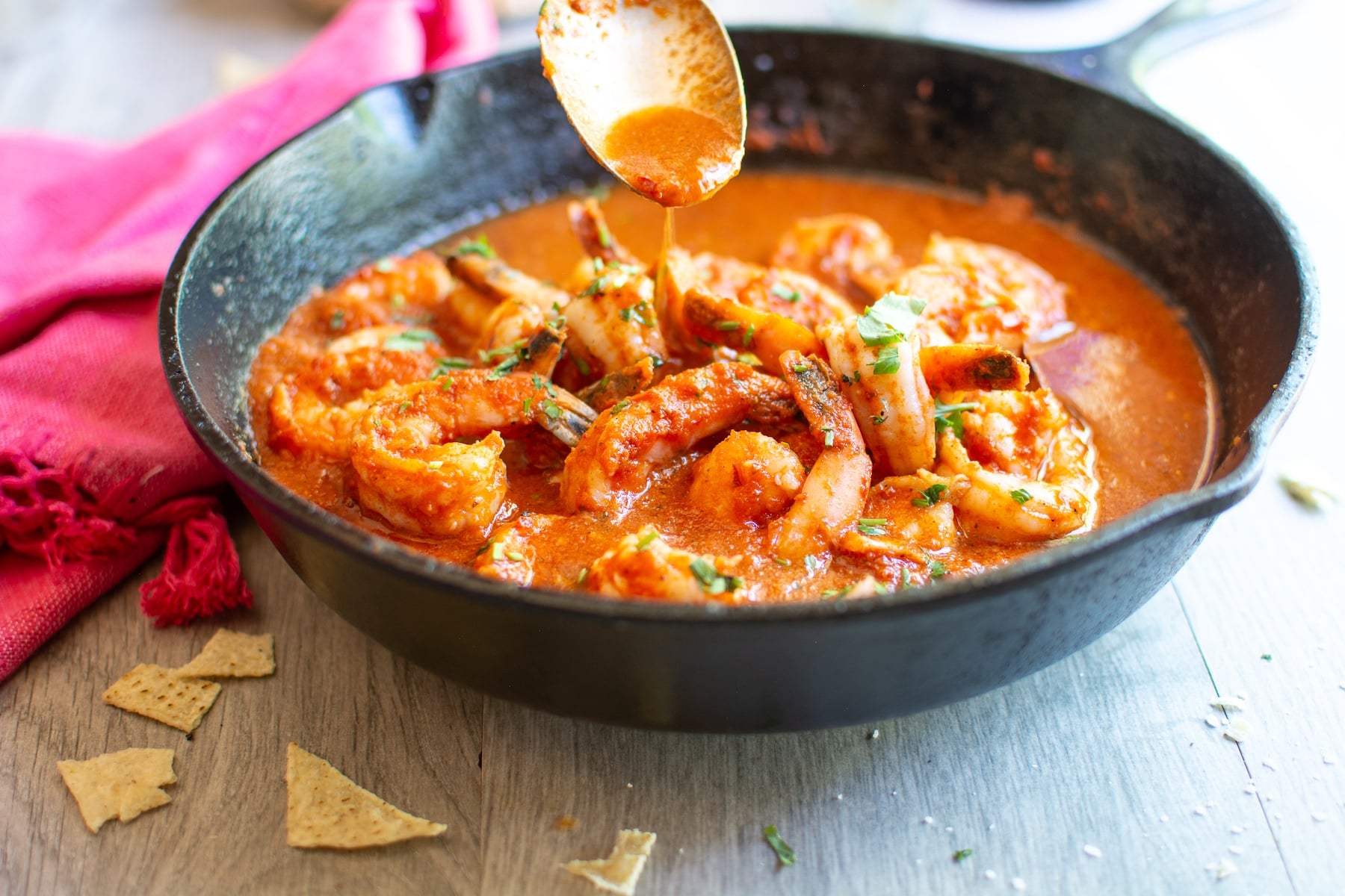shrimp in a cast iron skillet with a spoon dripping sauce