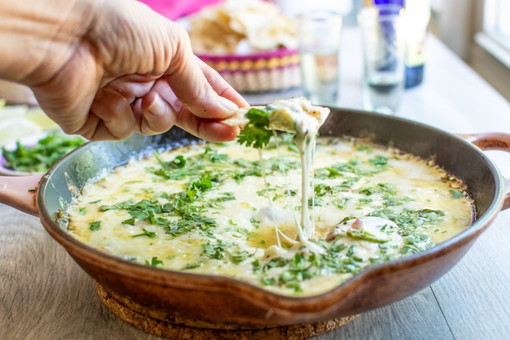 a hand dipping a chip in queso flameado