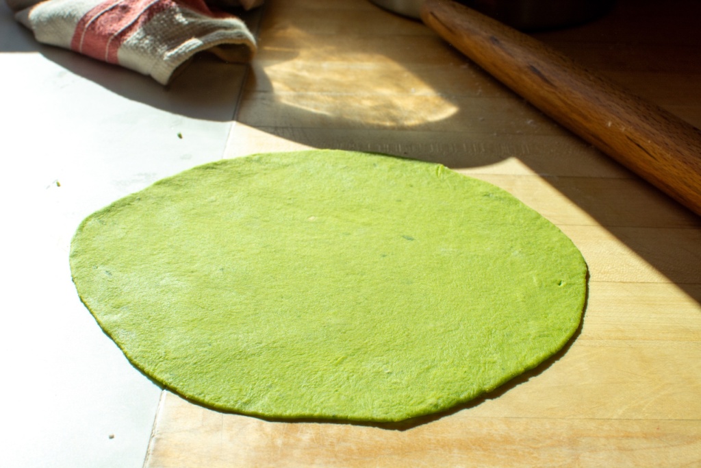 a green tortilla rolled out on a counter